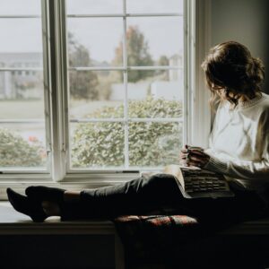 A woman sitting on a window sill reading a book
